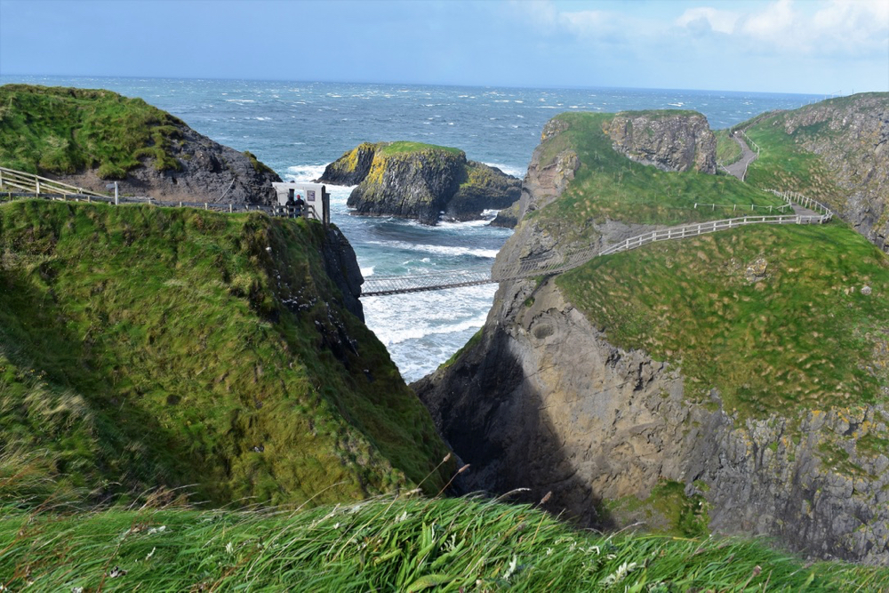 De beroemde brug van Carrick-a-Rede met groene heuvels en een woeste zee