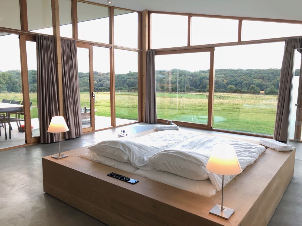 Een groot tweepersoons bed gericht op de grote ramen met uitzicht over de weilanden