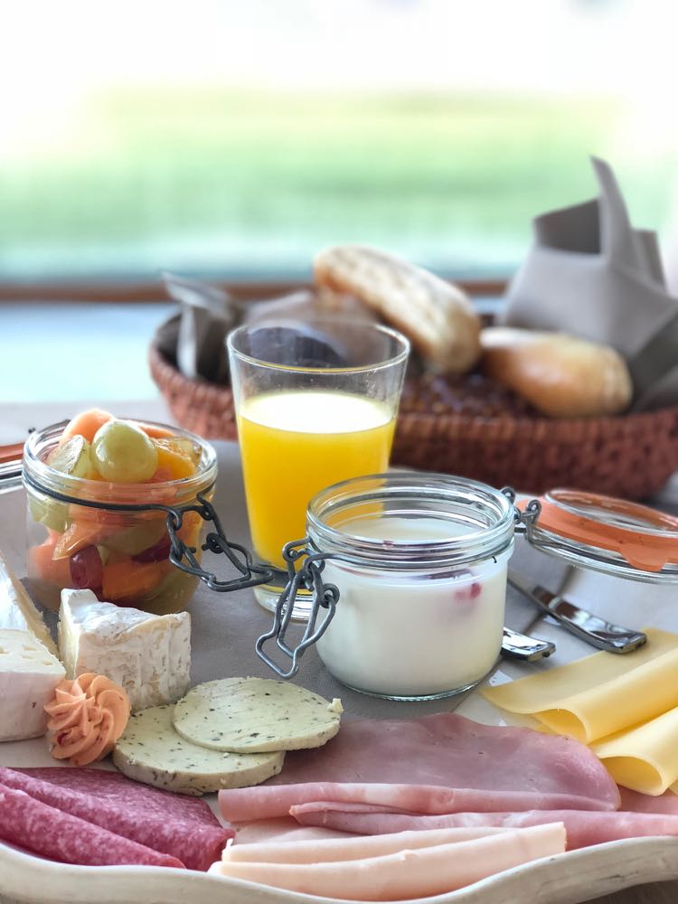 Ontbijt met sinasappelsap, yoghurt, broodjes en beleg.