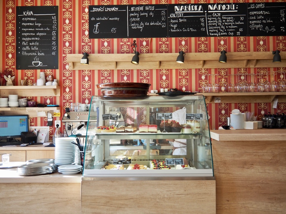 Vitrine met taartjes en een kleurrijk behang met daarop krijtborden met het menu