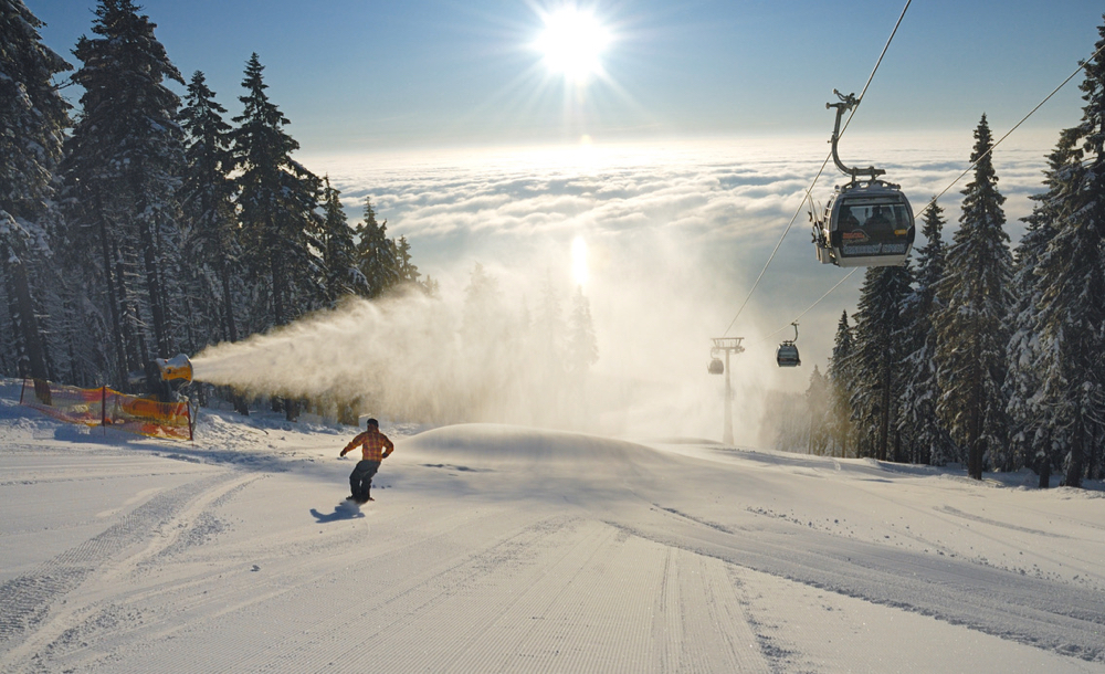 Een piste met tegenlicht, een skiër, cabinelift en een sneeuwkanon