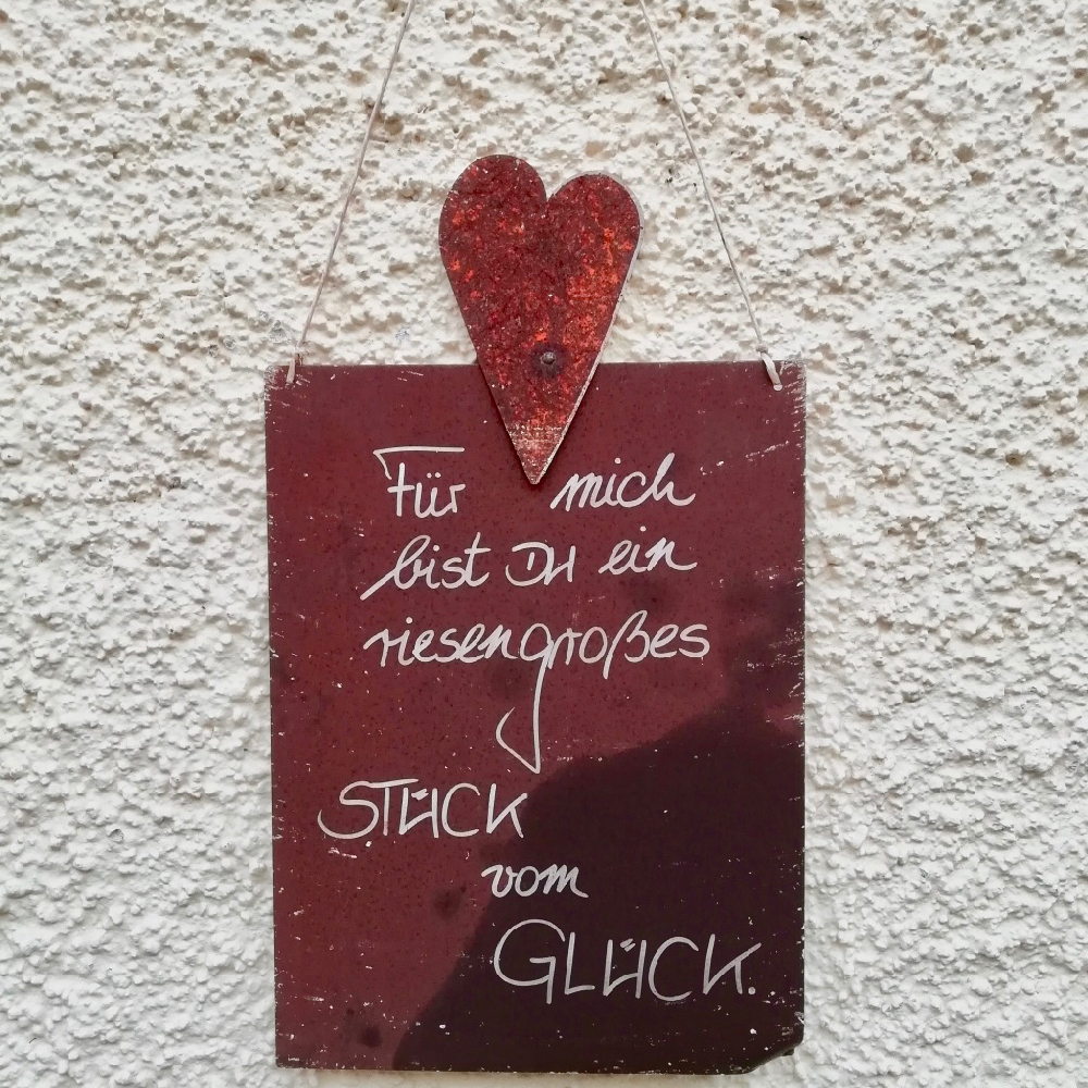 Een rood houten bordje op een witte muur