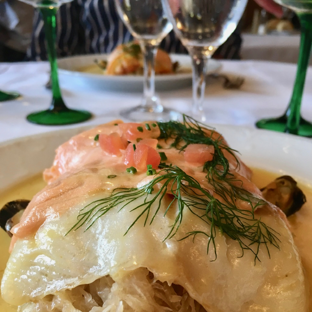Een bord met zuurkool met daarboven zalm en glazen wijn ernaast