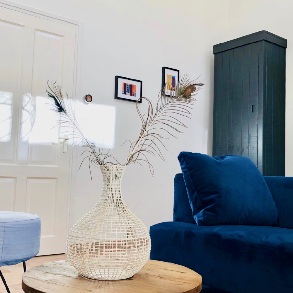 Lichte woonkamer met blauwe bank, ronde houten tafel en lichtblauwe poef.