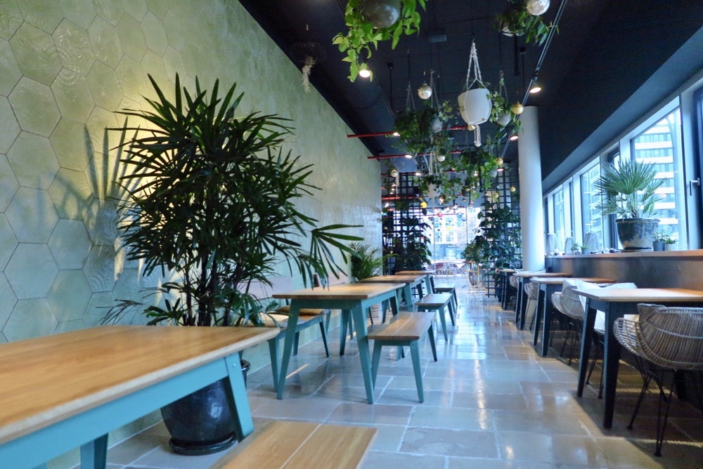 Houten tafels met blauw metalen frame en banken met grote planten ertussen bij restaurant picnic