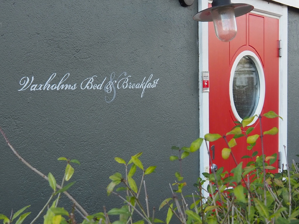 Zwarte muur met de tekst van de B&B Vaxholm en een rode deur