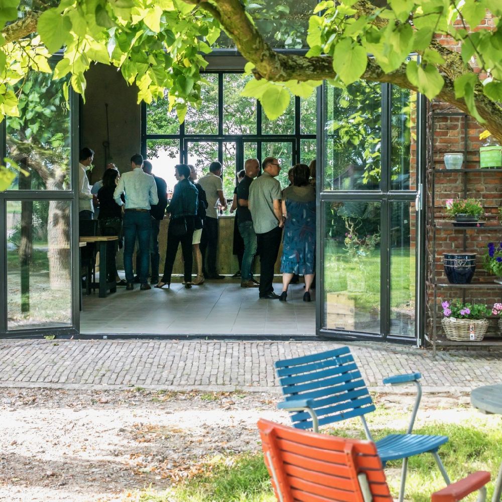 Schuur met opengeslagen metalen deuren, groep mensen aan het borrelen