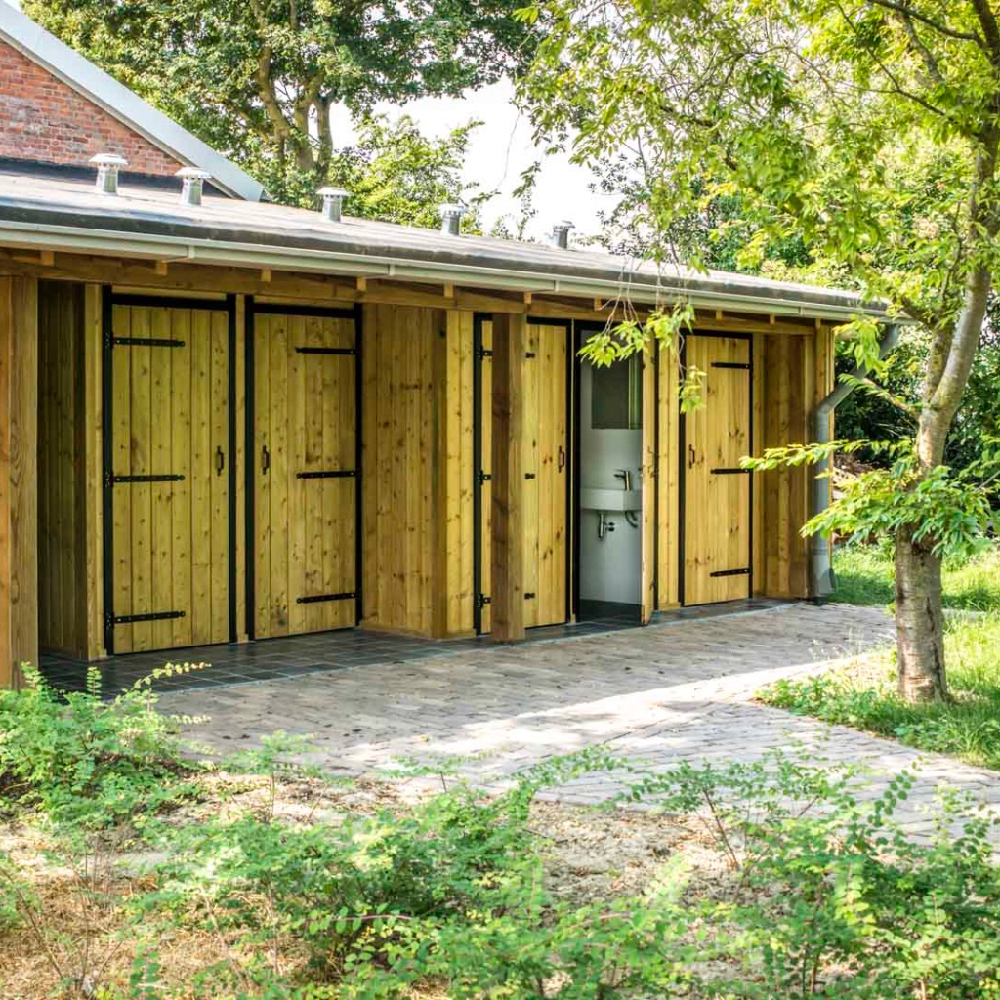 Houten sanitairgebouw met bomen eromheen