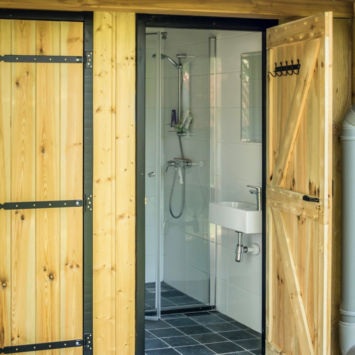 Nieuw sanitairgebouw met moderne douche en houten deuren