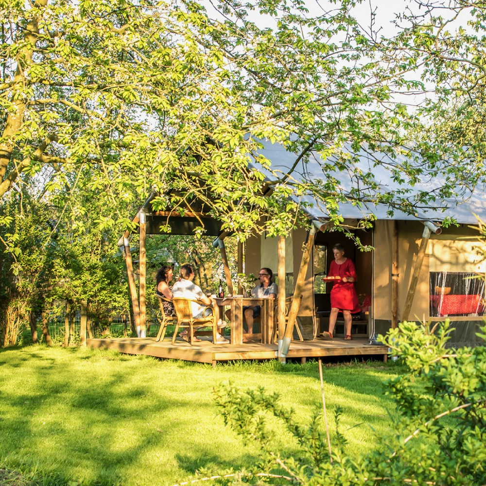 Safaritent tussen de bomen met mensen aan tafel op de veranda
