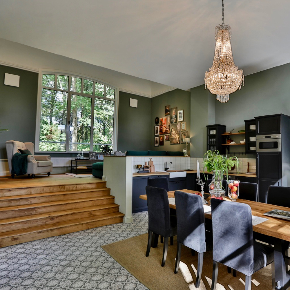 Doorkijk van eettafel met kroonluchter naar zithoek op verhoging, paar treden