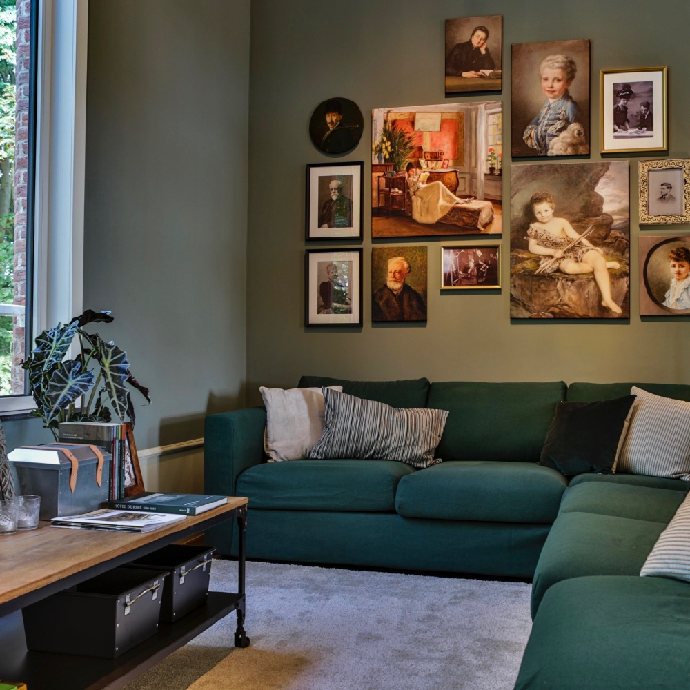 Zithoek met groene hoekbank, een salontafel en een verzameling schilderijen aan de wand