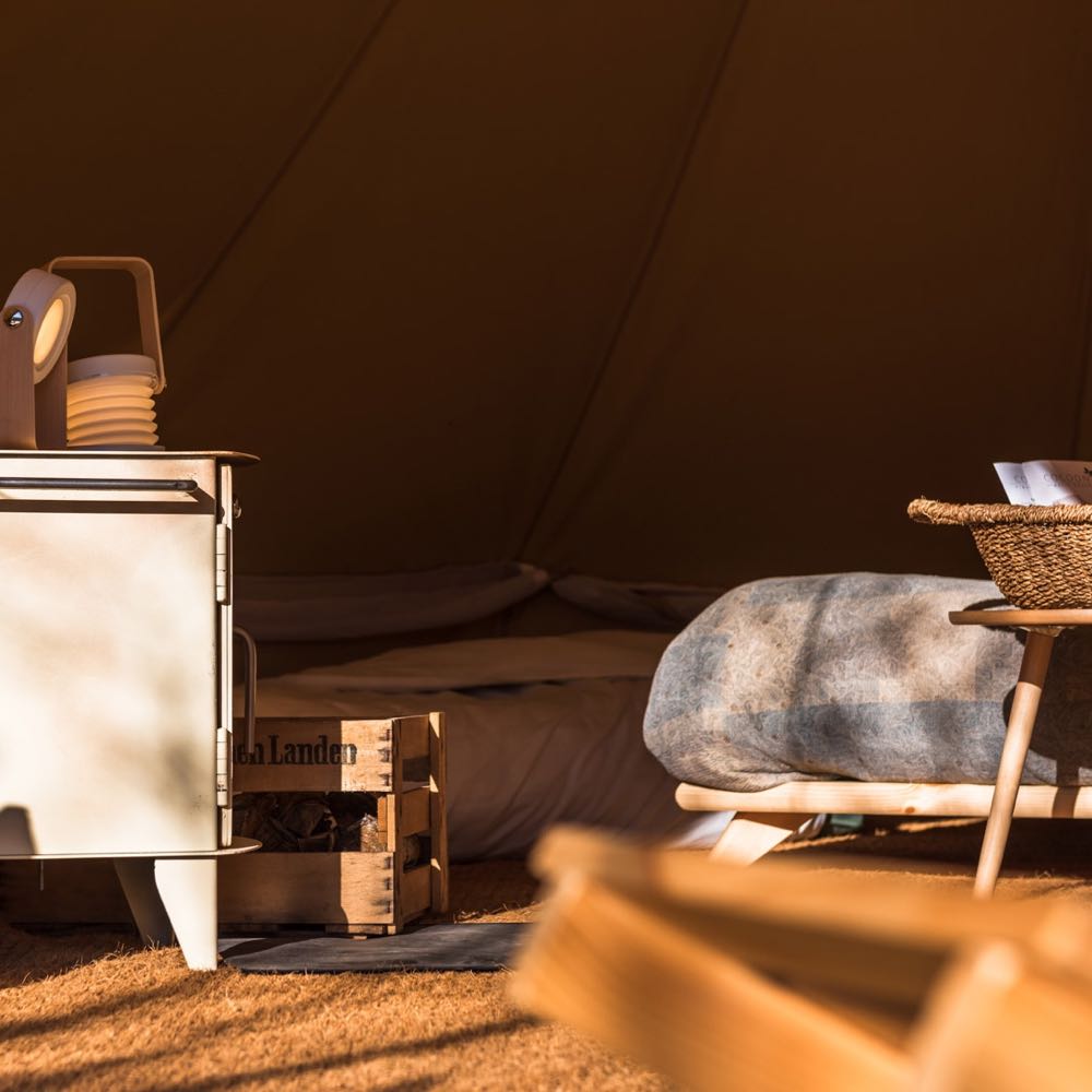 Een bell tent ingericht met een tweepersoons bed en houtkachel