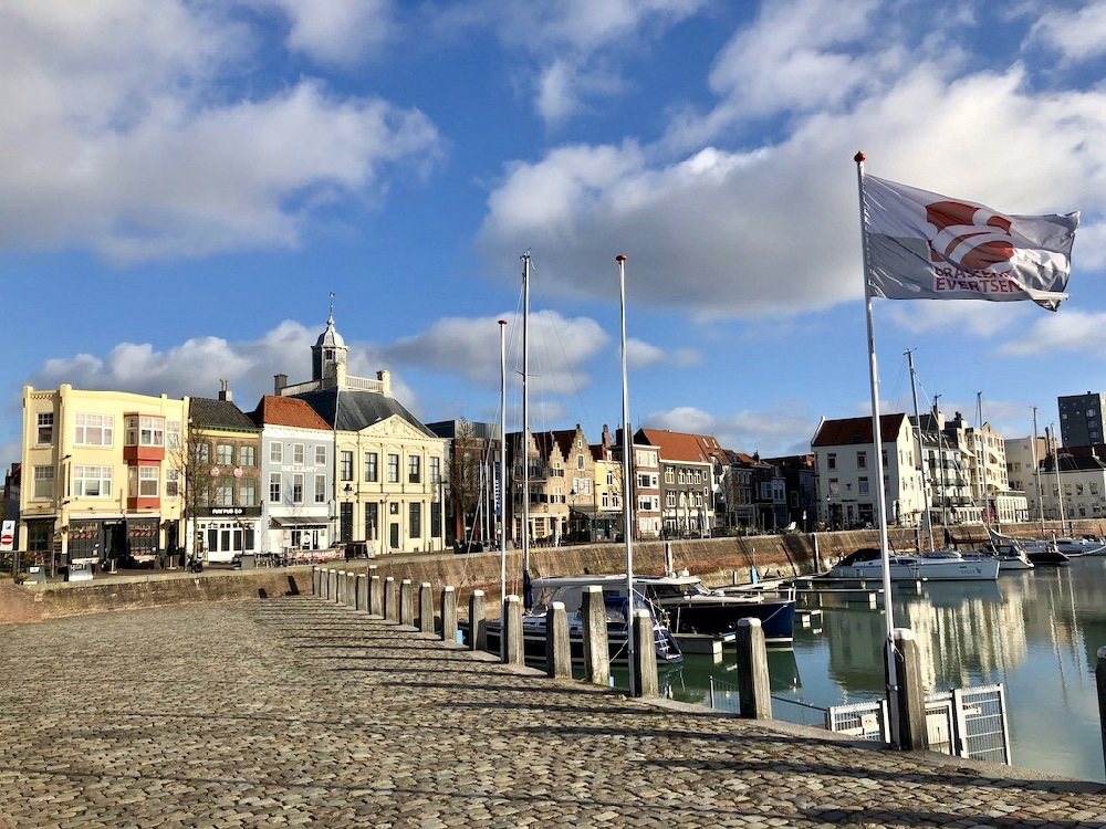 Kade van de haven met zeilboten, kleurrijke gevels en een wapperende vlag