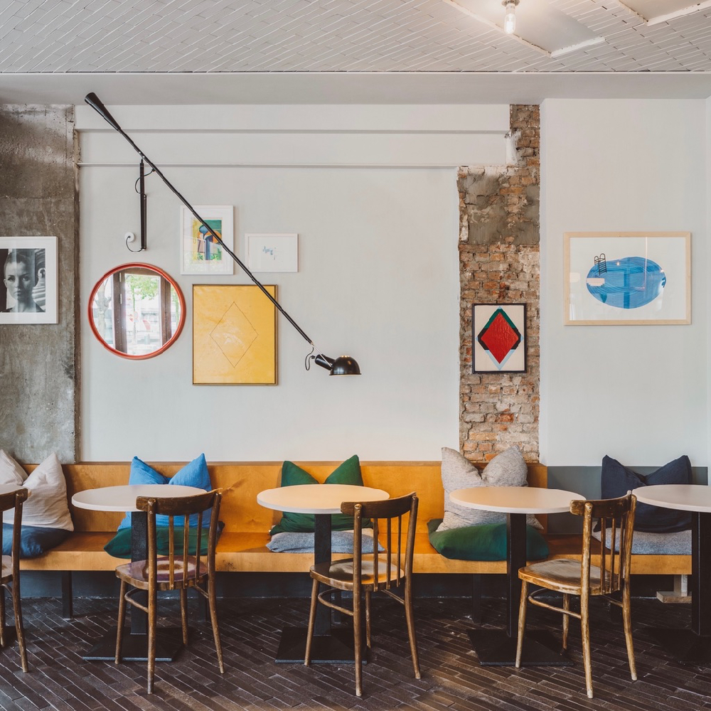 Houten bank langs de muur met ronde tafeltjes en gekleurde kussens op de bank