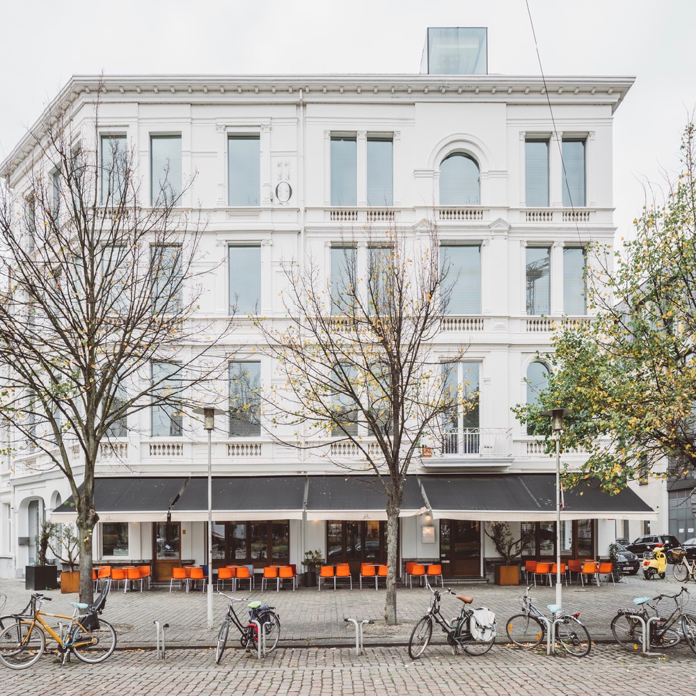 Witte gevel van een hotel, oranje stoelen op het terras