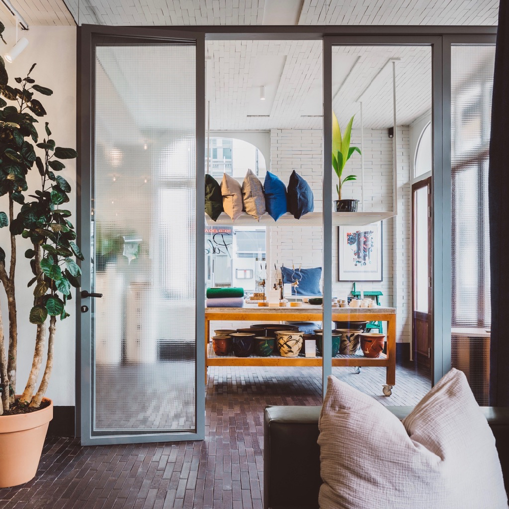 Grote stalen deuren met erachter een winkelruimte met een tafel vol woonaccessoires en kussens