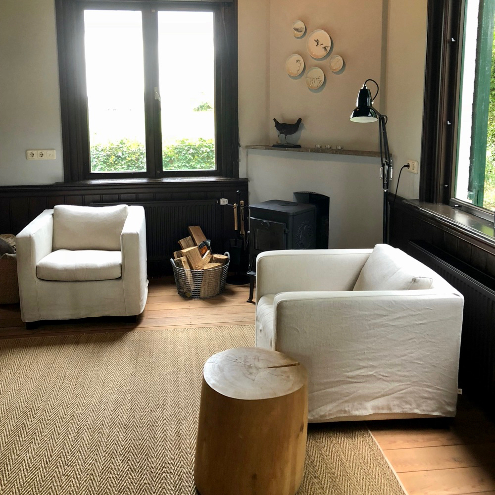 Twee fauteuils met linnen bekleding bij een zwarte houtkachel