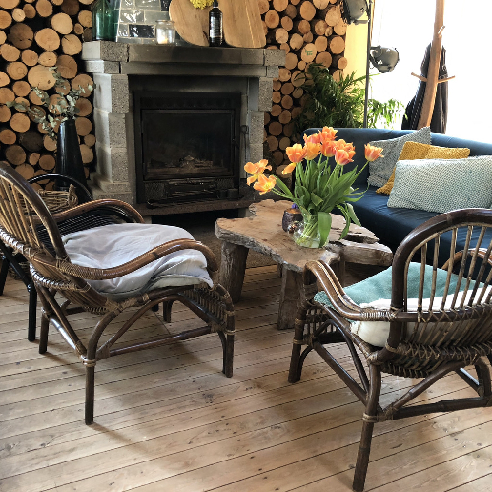 Gezellig zitje bij een haard, twee rotanstoelen en een grote vaas oranje tulpen op tafel