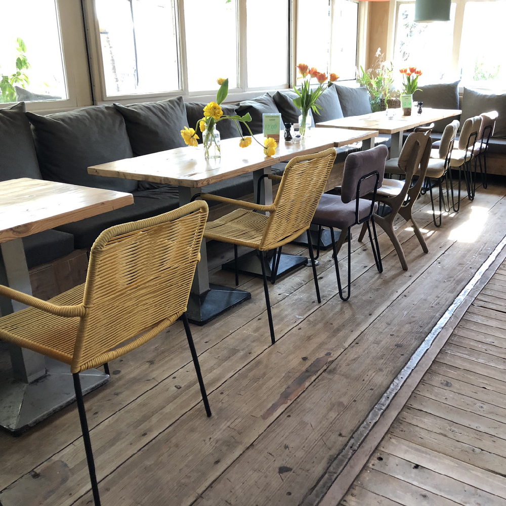 Lange rij tafels met een bank met kussens langs de ramen en verschillende stoelen