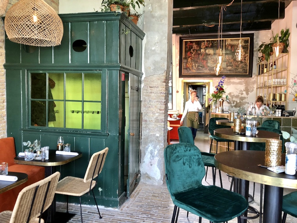 Eigentijds interieur met oranje banken, rieten stoelen, een groen houten garderobekast en robuuste muren