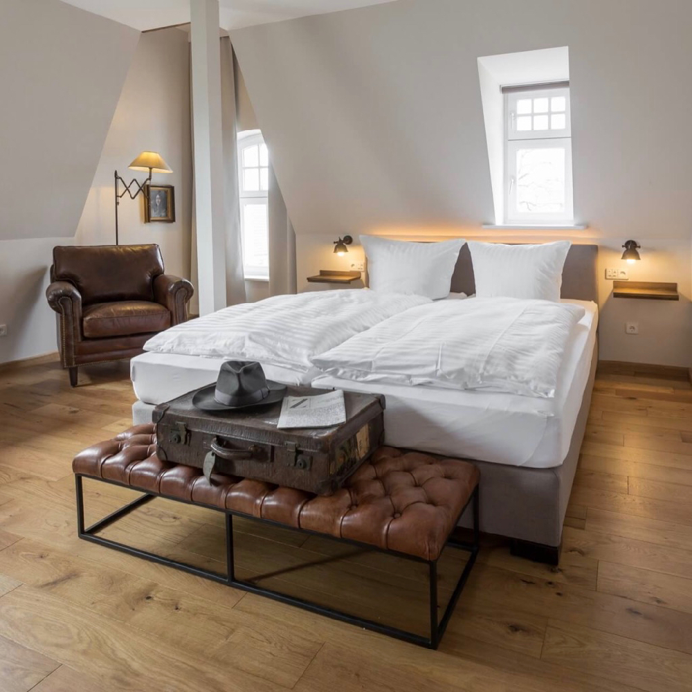 Hotelkamer met leren fauteuil en een vintage koffer op een bankje