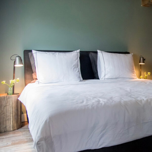 Opgemaakt tweepersoons bed met boomstronken als nachtkastjes