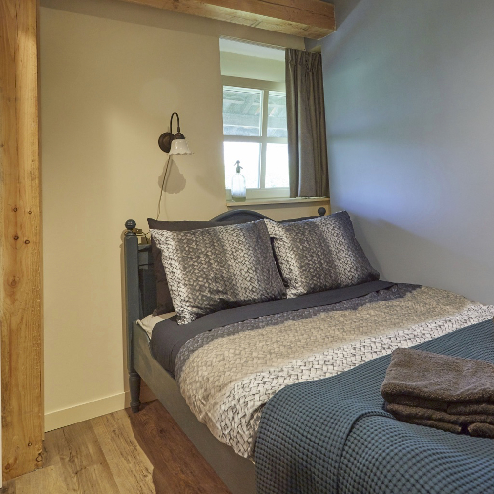 Opgemaakt bed met sprei en stapeltje handdoeken