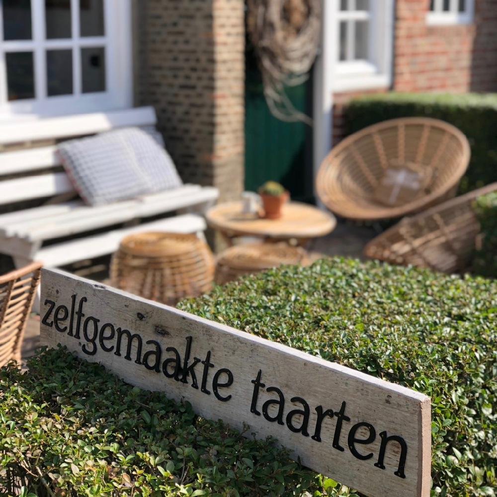 Een bordje naast een terras. Op het bordje staat "zelfgemaakte taarten"