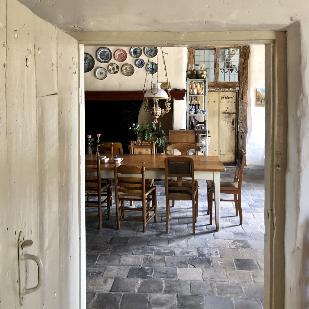 Een lange houten tafel op een stenen vloer, met zeven zichtbare stoelen er om heen