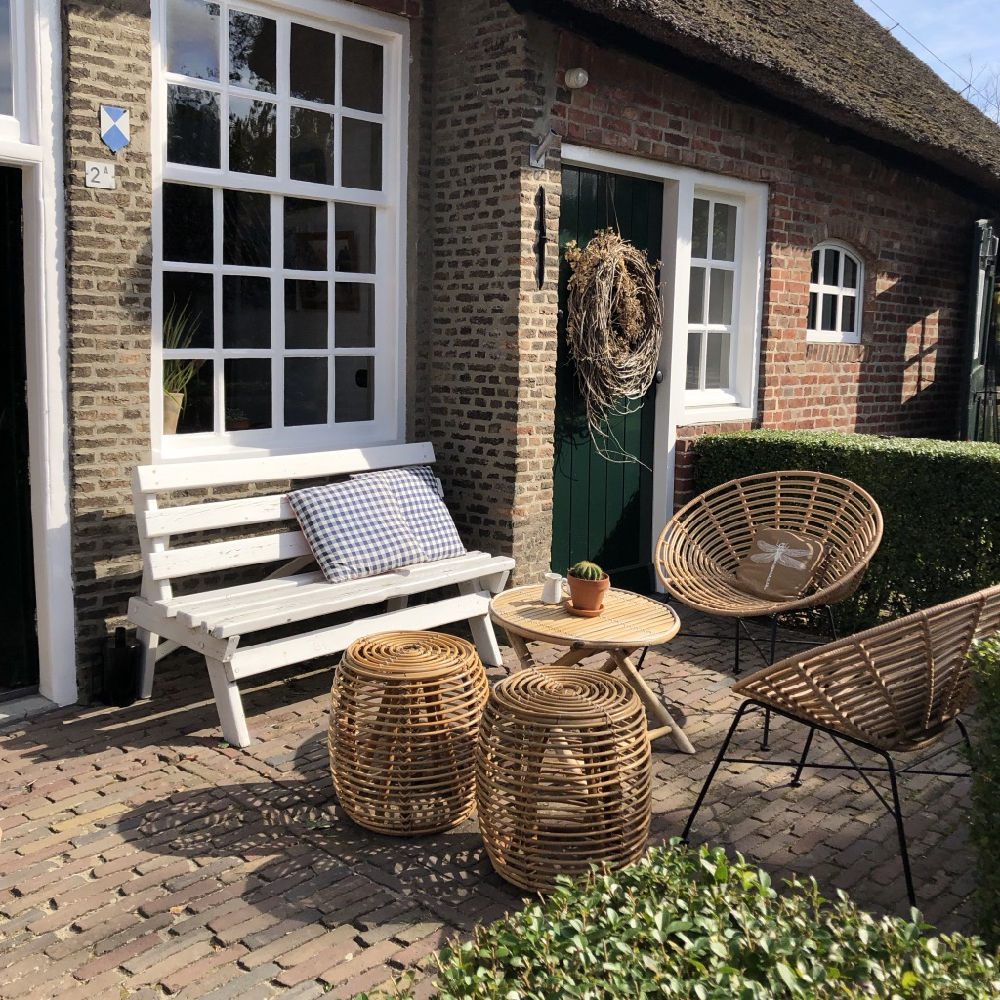 Een terrasje met een wit bankje en twee houte stoeltjes