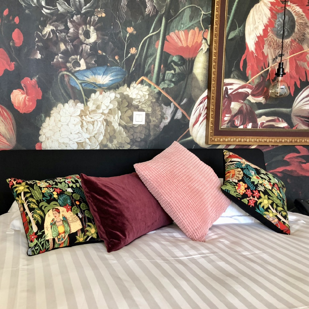 Hotelbed met gekleurde kussens en bloemenbehang