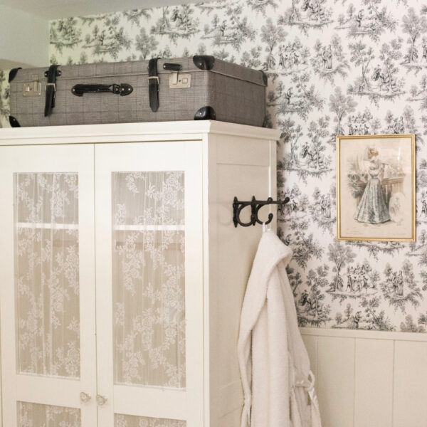 Slaapkamer met romantisch behang, een witte kast en koffer op de kast