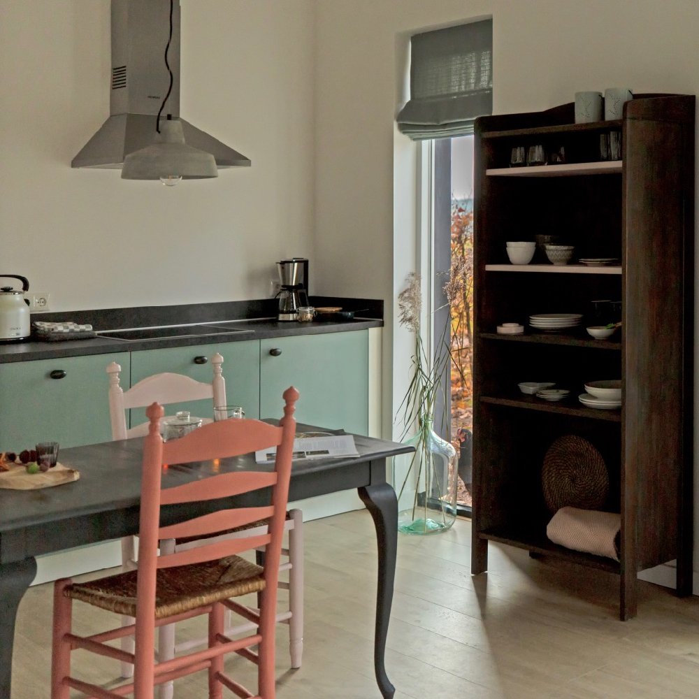 Eettafel met rode en roze stoel, mintgroene keuken