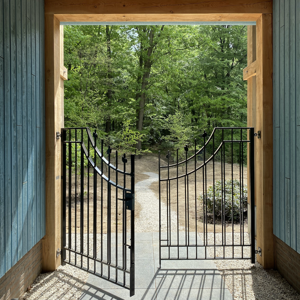 Geopende poort met wandelpad het bos in.