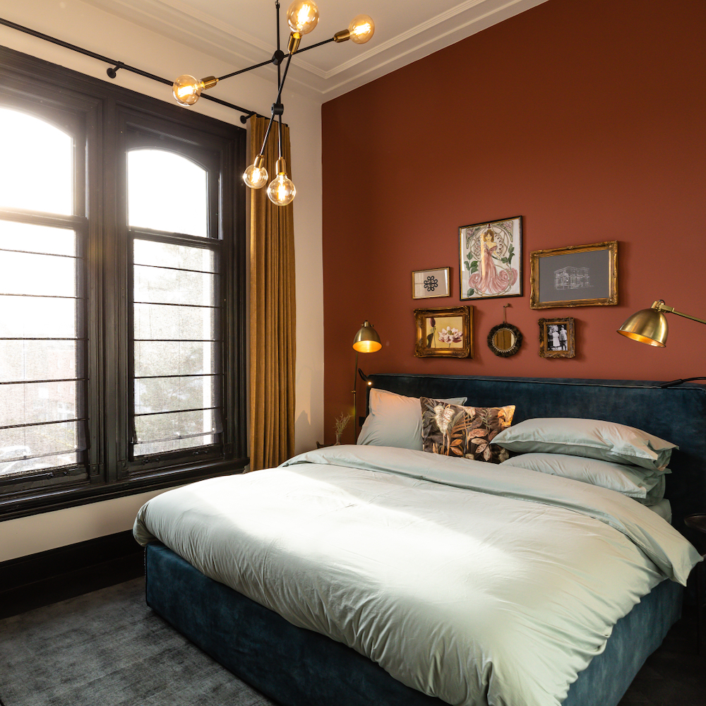 Luxe suite met roodbruine wand en lijstjes boven het bed in het boutique hotel