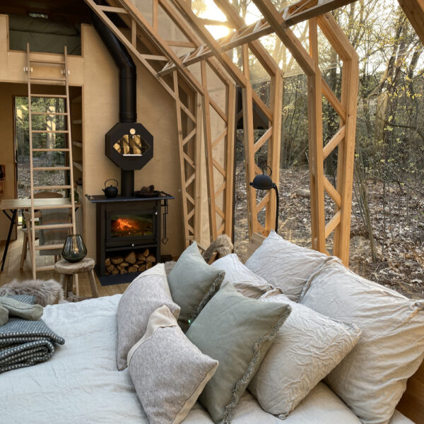 Opgemaakt bed met stapel kussens bij brandende houtkachel