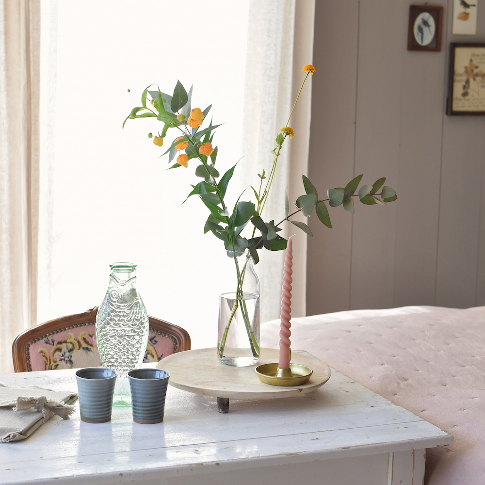Wit houten tafeltje met een vaasje bloemen en gedraaide kaars
