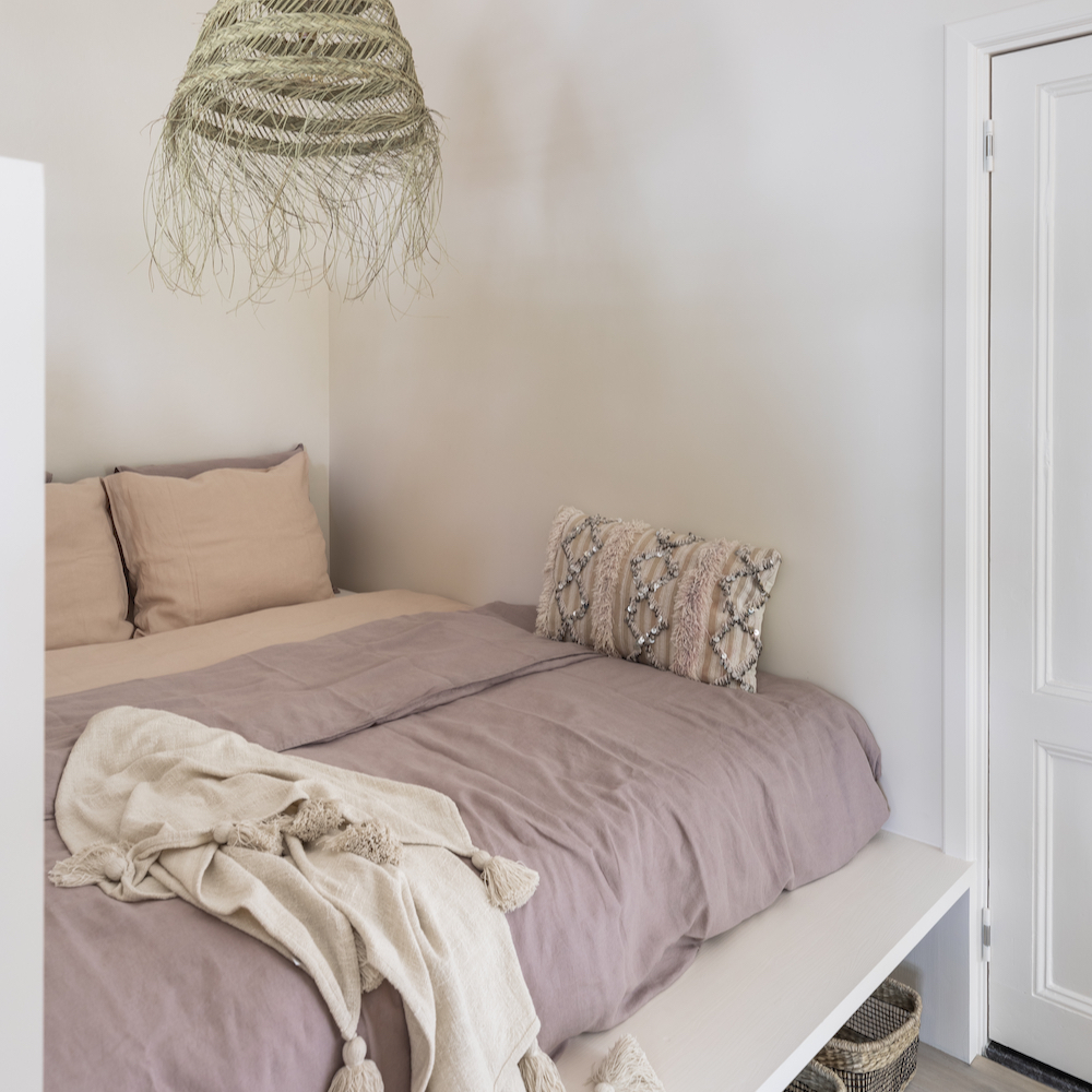 Tweepersoons bed met roze beddengoed en rieten lamp