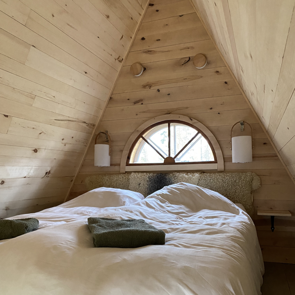 Bed onder een schuin dak in een duurzaam vakantiehuisje in Zweden.