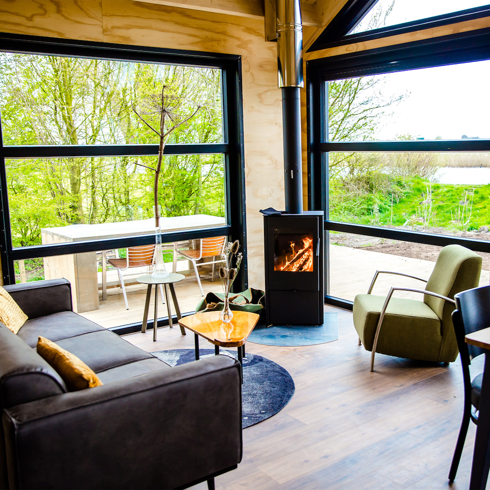 Zithoek voor de grote ramen met brandende houtkachel.