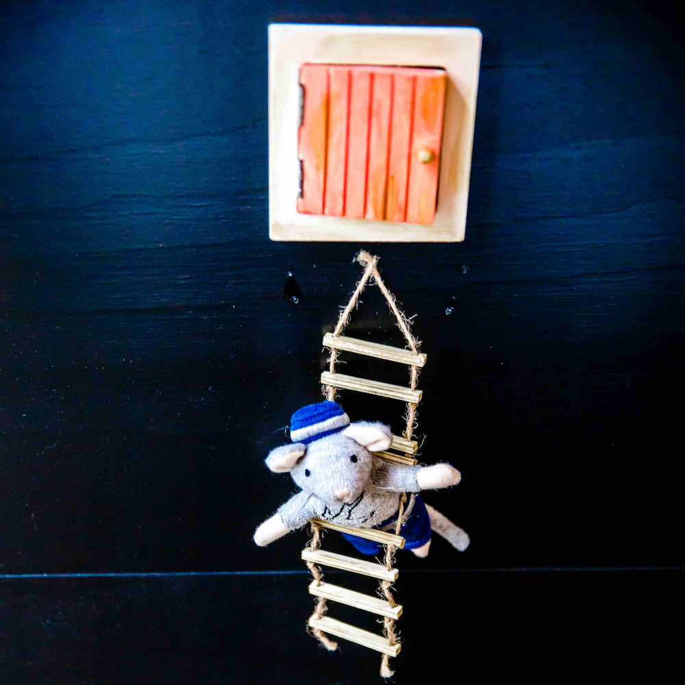 Muisje op een trappetje bungelt aan een luikje in de wand.