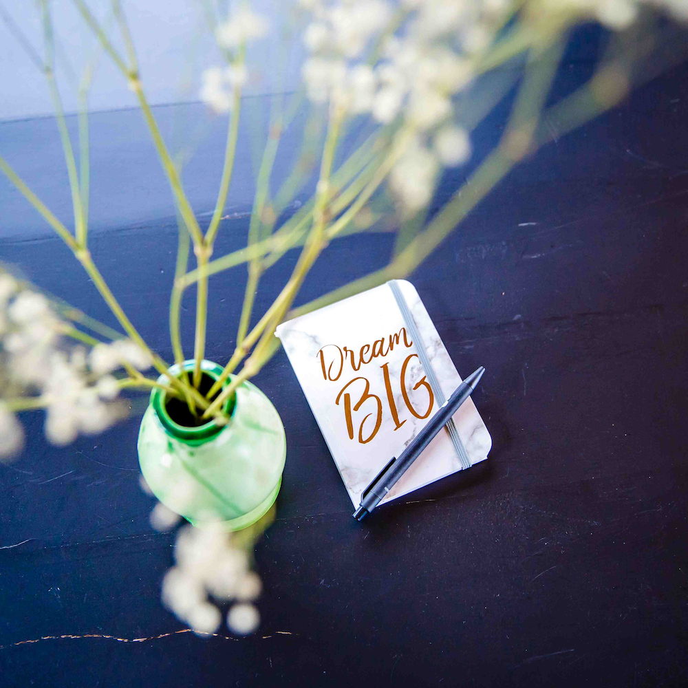 Groen vaasje op een blauwe tafel en een schriftje met de tekst 'dream big'.