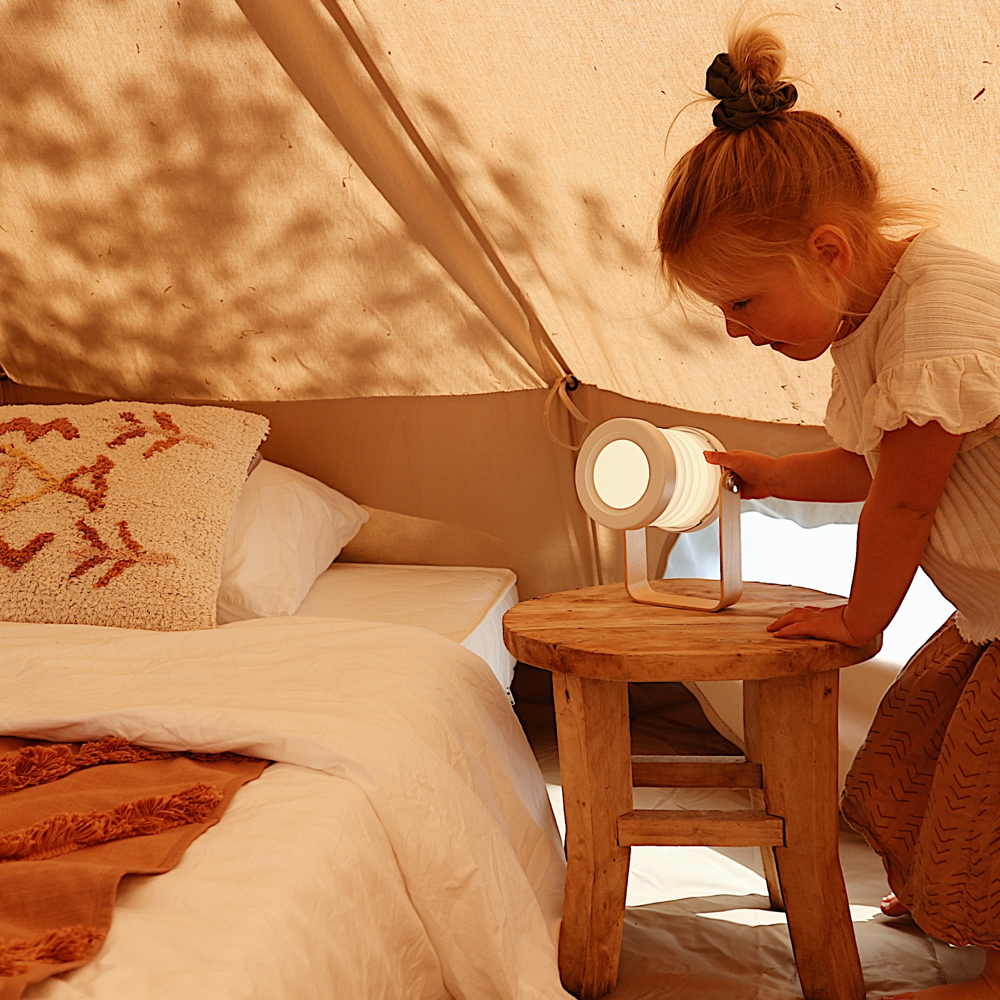 Meisje bij lampje naast het bed in de bell tent
