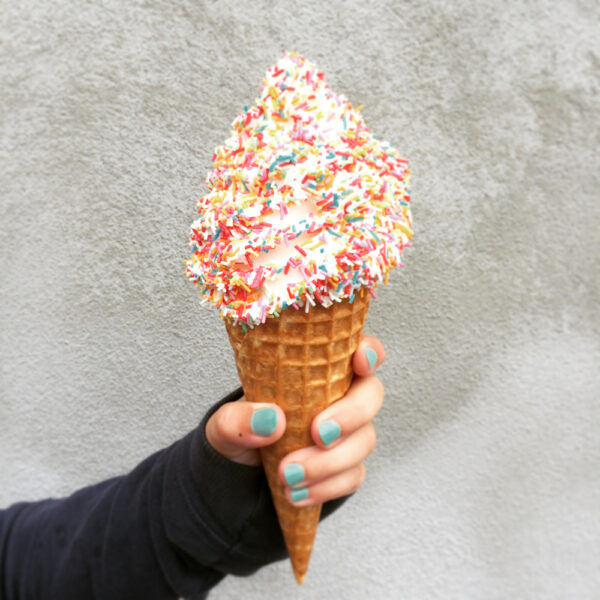 Ein Eis in der Hand, blauer Nagellack und Sprenkel auf dem Eis