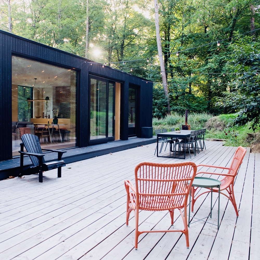 Schwarzes modernes Ferienhaus mit großer Terrasse mit roten Rattanstühlen
