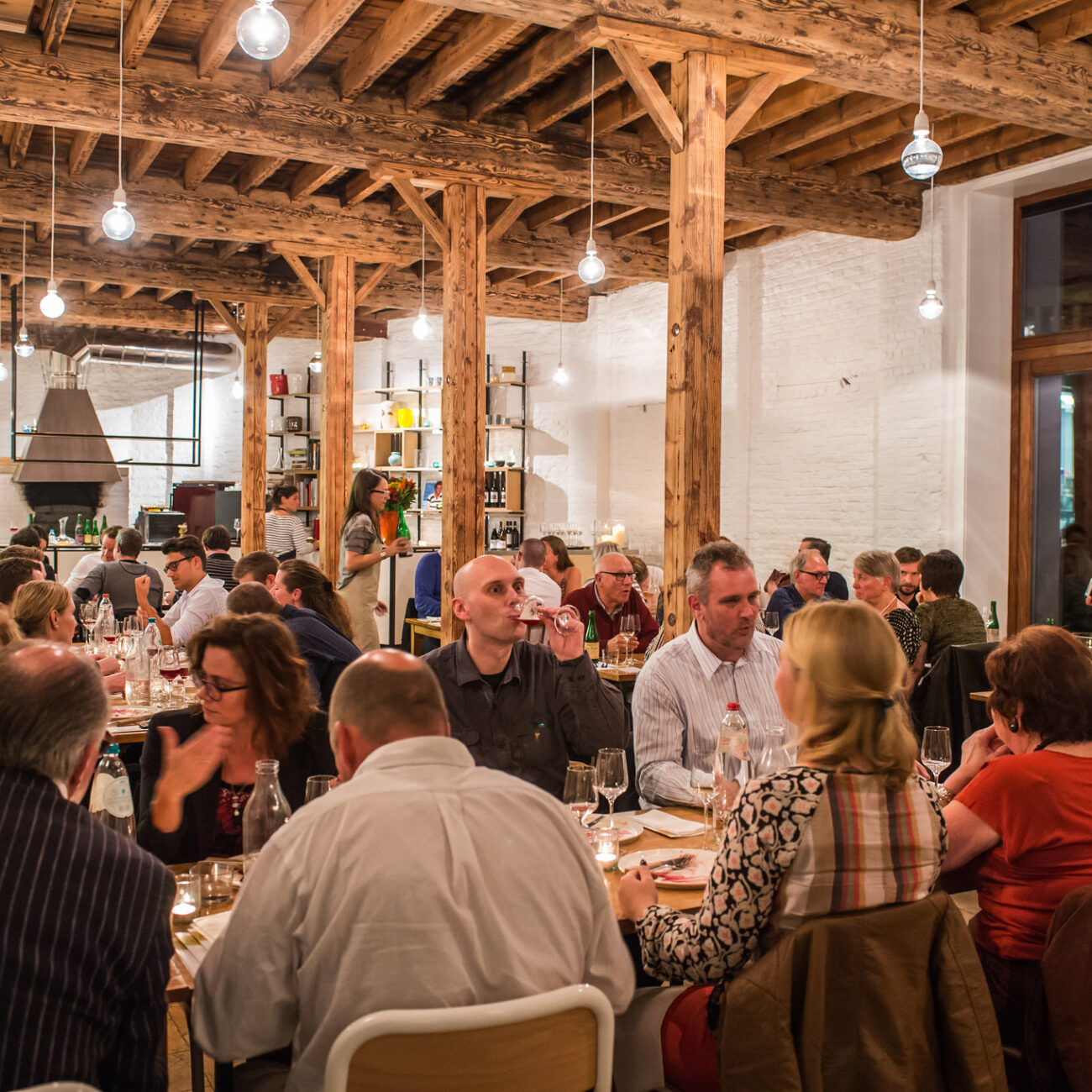 Ein Restaurant mit langen Tischen voller Gäste. Darüber robuste Holzbalken