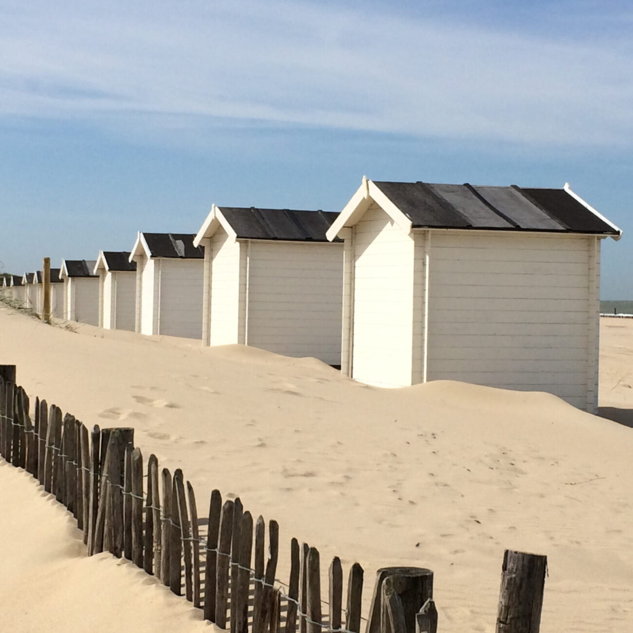 Eine Reihe von weißen Strandhäusern im lockeren Sand. Am Strand bei Groede in Zeeland.