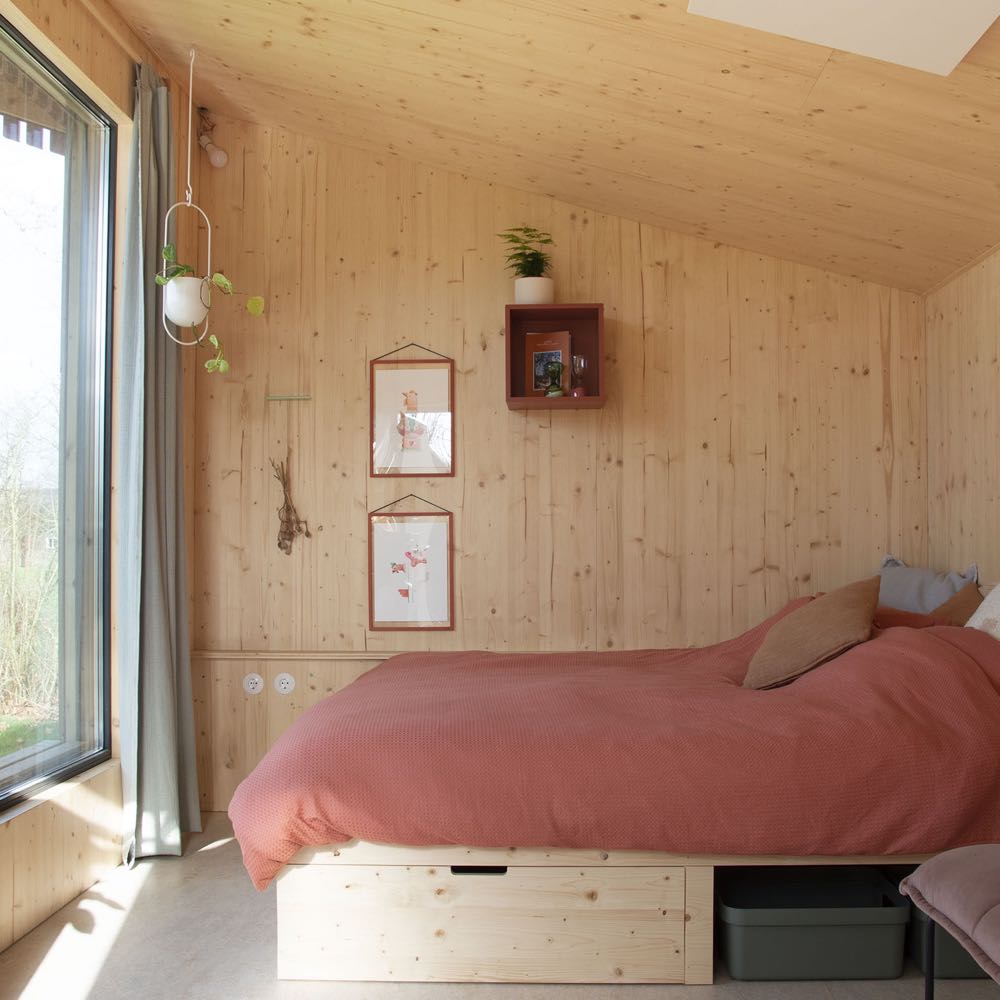 Doppelbett vor einem großen Fenster in einem kleinen Haus