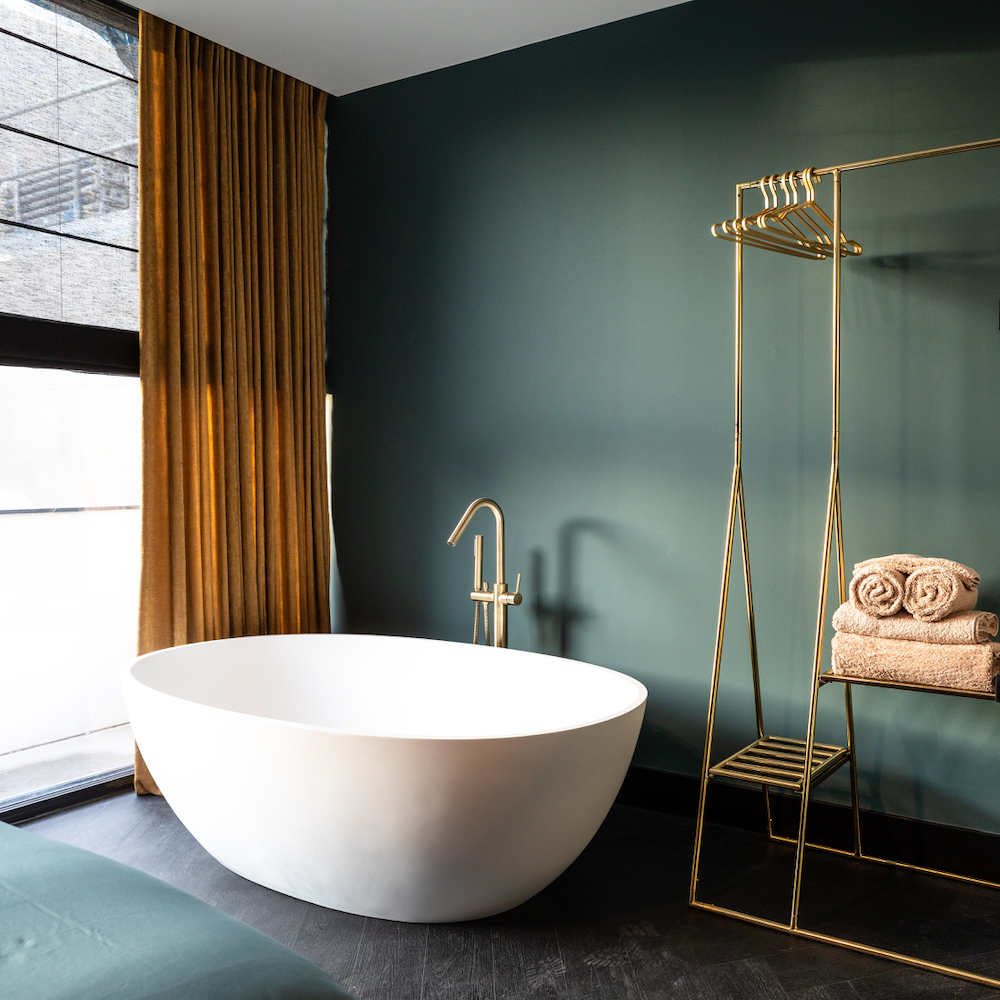Freistehende Designerbadewanne mit grüner Wand in einem Boutique-Hotel